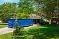 An empty blue dumpster in the driveway of a house with its garage door open in a residential community Royalty Free Stock Photo