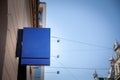 Empty blue square shop signboard hanging on a building facade, visible against a clear sky in a European city street, ideal for Royalty Free Stock Photo