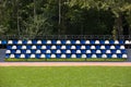 Empty blue and white seats in a football or soccer stadium. Grass field and plastic chairs, open door sports arena Royalty Free Stock Photo