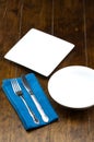 Empty bowl and square dish with fork, knife, napery on wood table. Royalty Free Stock Photo