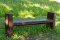 Empty brown bench on green grass and yellow flowers with bright sun light in the city park during summer sunny day. Public chair Royalty Free Stock Photo