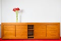 Empty brown wooden commode with three flowers on red car carped and next to white wall Royalty Free Stock Photo