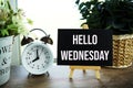 Hello Wednesday text message on wooden easel and alarm clcok on wooden background Royalty Free Stock Photo