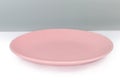 Empty ceramic pink flat plate on white surface, side view