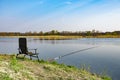 An empty chair and fishing rod on the lake coast in the morning. Green grass near large lake, blue sky, early hours Royalty Free Stock Photo