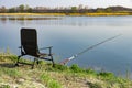 An empty chair and fishing rod on the lake coast in the morning. Green grass near large lake, blue sky, early hours Royalty Free Stock Photo