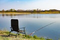 An empty chair and fishing rod on the lake coast in the morning. Green grass near large lake, blue sky, early hours Royalty Free Stock Photo