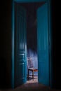 Empty chair in light behind blue massive vintage doors indoor.