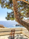 Empty chair on terrace in front of aegean sea under shadow of pine tree, Sifnos island, Greece