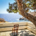 Empty chair on terrace in front of aegean sea under shadow of pine tree, Sifnos island, Greece