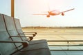 Empty chairs in the departure hall at airport on background of airplane taking off at sunset. Travel concept Royalty Free Stock Photo