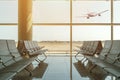 Empty chairs in the departure hall at airport on background of airplane taking off at sunset. Travel concept Royalty Free Stock Photo