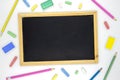 Empty chalkboard with art supplies on white background. Blackboard and colorful chalk flat lay photo. Royalty Free Stock Photo