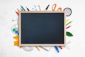 Empty chalkboard for promo text surrounded by school supplies on white desk Royalty Free Stock Photo