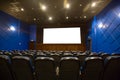 Empty cinema auditorium with empty white screen. Empty rows of blue theater or movie seats