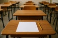Empty classroom filled with desks, with paper and pencil on a desk in the foreground Royalty Free Stock Photo