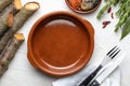 Empty clay pot. On white wooden background. Of rustic aspect it includes spices rosemary, laurel, chilli peppers and cutlery.