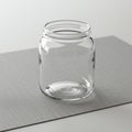An empty, clear glass jar is placed on a gray textured surface. The jar is cylindrical wit Royalty Free Stock Photo