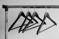 Empty clothes hangers on metal rail against grey background. Rectangular metal clothing rail with empty black wooden