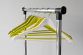 Empty clothes hangers on metal rail against grey background. Rectangular metal clothing rail with empty color wooden