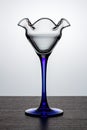 Empty cocktail glass with blue thin and high leg on dark wooden surface in white backlight Royalty Free Stock Photo