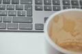 Empty coffee cup with blurred espresso residue in foreground and sharp laptop keyboard behind it creating a modern workspace Royalty Free Stock Photo