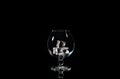 An empty cognac glass with ice cubes on a black background with reflection