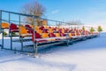 Empty Colorful Football Soccer Stadium Seats in the Winter Covered in Snow - Sunny Winter Day with Clear Blue Sky in the Royalty Free Stock Photo