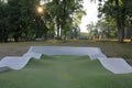 Empty concrete skateboard park at sunrise. Playground in the background, with rays of sunrise shinging through trees Royalty Free Stock Photo