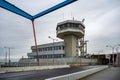 An empty control tower stands next to a multi-story building, with a bridge and overpass in the background under a cloudy sky, Royalty Free Stock Photo