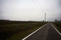 Empty country road bordered by stream of water and electricity pylons on a cloudy day in the italian countryside Royalty Free Stock Photo