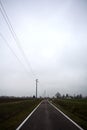 Empty country road bordered by stream of water and electricity pylons on a cloudy day in the italian countryside Royalty Free Stock Photo