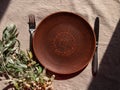 Empty craft handmade clay plate with fork knife on tablecloth. Table place hand crafted dish Natural home interior decor Royalty Free Stock Photo
