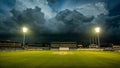 Empty cricket stadium pitch illuminated by bright stadium floodlights against a dramatic backdrop of dark menacing storm clouds Royalty Free Stock Photo