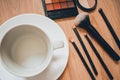 Empty cup on wooden background with makeup brushes and an eyeshadow palette. Autumn flatlay.