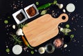 Empty cutting board and pepper, bay leaf, rosemary, onions, Himalayan salt, olive oil, soy sauce on a black backg Royalty Free Stock Photo