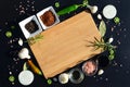 Empty cutting board and pepper, bay leaf, rosemary, onions, Himalayan salt, olive oil, soy sauce on a black backg Royalty Free Stock Photo