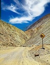 Empty dangerous sandy dirt road in barren arid desert rocky stony landscape to pacific coast, old rusty steep hill downwards sign