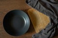 Empty dark black plate with wood cutting board and napkin. Black kitchen utensils set on wooden table. Top view, flat lay Royalty Free Stock Photo