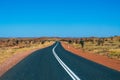 Empty dark road leading through red sanded Australian landscape towards Karijini National Park