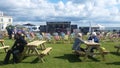 Empty deck chairs with fabric blowing in the wind in front of Cookery Theatre Stage on a green at a festival