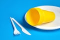 Empty disposable plastic tableware on blue background. White plate fork, knife and yellow plastic glasses Royalty Free Stock Photo