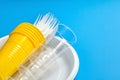 Empty disposable plastic tableware on blue background. White plate forks, knives, yellow and transparent plastic glasses Royalty Free Stock Photo