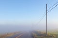 Empty, foggy, rural farm country road in the early morning sunlight with powerlines Royalty Free Stock Photo