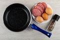 Frying pan, sliced sausage, brown eggs in white plate, jar with condiment on wooden table. Top view Royalty Free Stock Photo