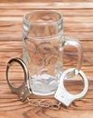 Empty glass for beer and handcuffs on wooden table. Alcohol dependence