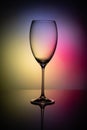 Empty glass goblet without wine on a thin leg stands on a mirror surface. Colorful background Royalty Free Stock Photo