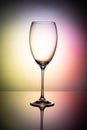 Empty glass goblet without wine on a thin leg stands on a mirror surface. Colorful background Royalty Free Stock Photo