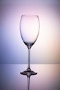 Empty glass goblet without wine on a thin leg stands on a mirror surface. Colorful purple background Royalty Free Stock Photo