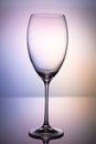 Empty glass goblet without wine on a thin leg stands on a mirror surface. Colorful purple  background Royalty Free Stock Photo